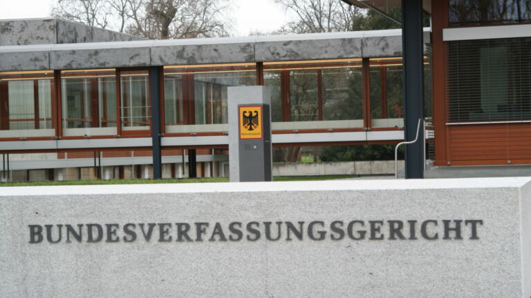 Auf einer Mauer steht "BUNDESVERFASSUNGSGERICHT" Im Hintzergrund ist ein flaches Gebäude zus sehen